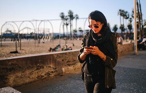 A woman walks near the beach and uses her smartphone
