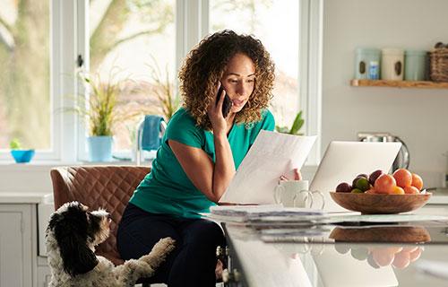 A woman uses her phone and laptop while her dog tries to get attention